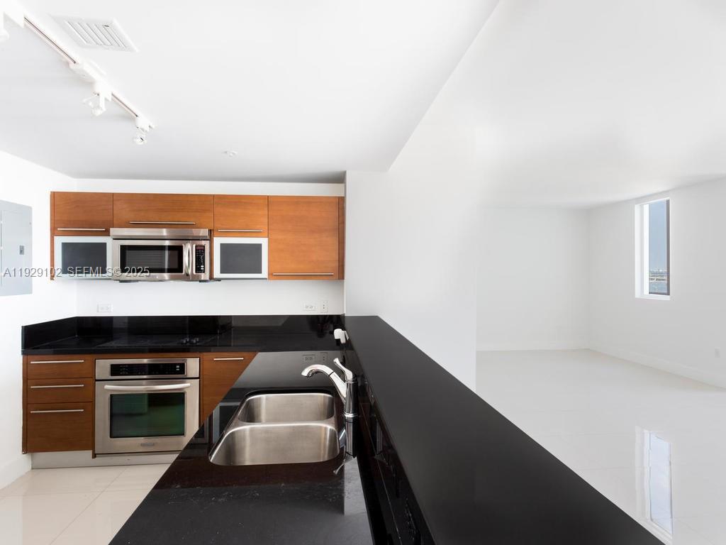 A modern kitchen features wood cabinets, black countertops, and stainless steel appliances — 244 Biscayne Blvd # 2402, Miami FL 33132, MIAMI, FL