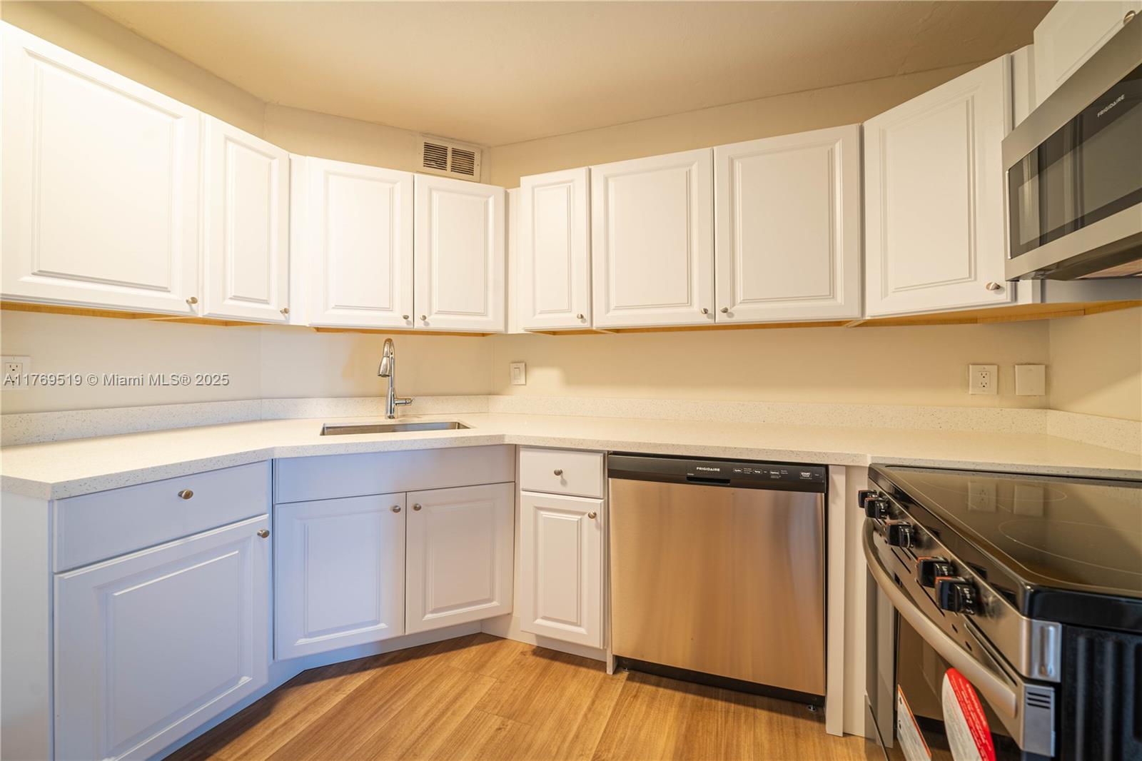 A kitchen features white cabinets, stainless steel appliances, and light countertops over wood-look flooring — 3301 Spanish Moss Ter # 802, Lauderhill FL 33319, LAUDERHILL, FL