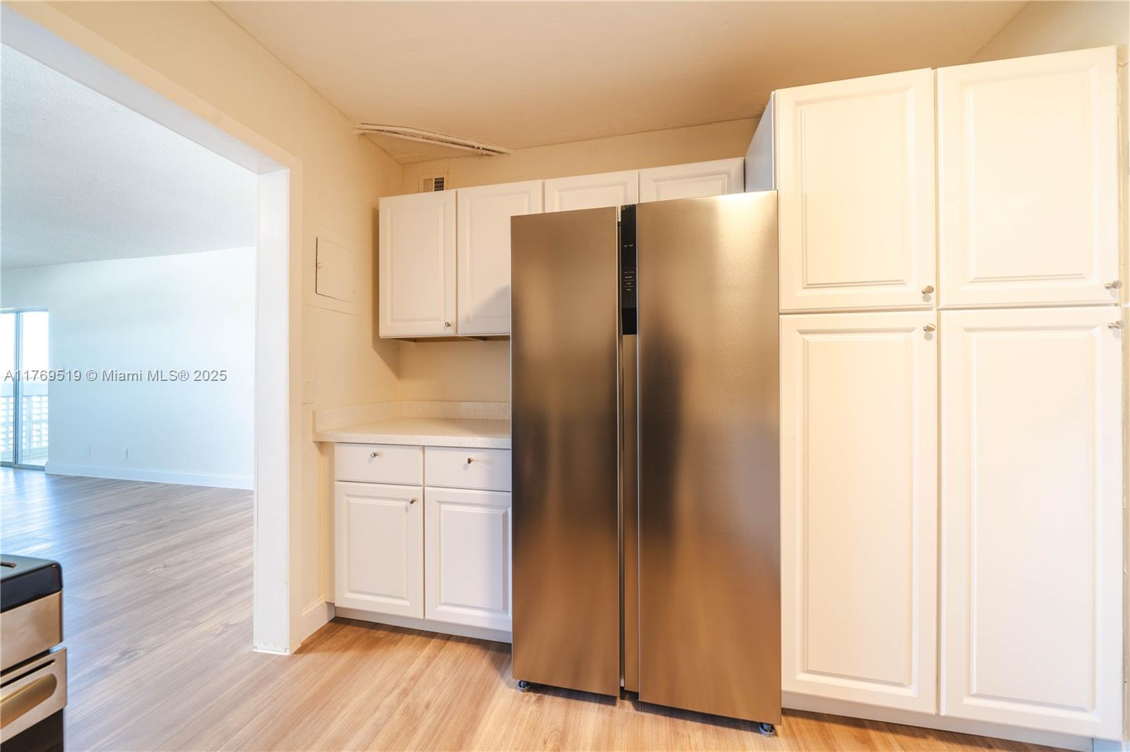 A kitchen features white cabinets, a stainless steel refrigerator, and light wood-look flooring — 3301 Spanish Moss Ter # 802, Lauderhill FL 33319, LAUDERHILL, FL