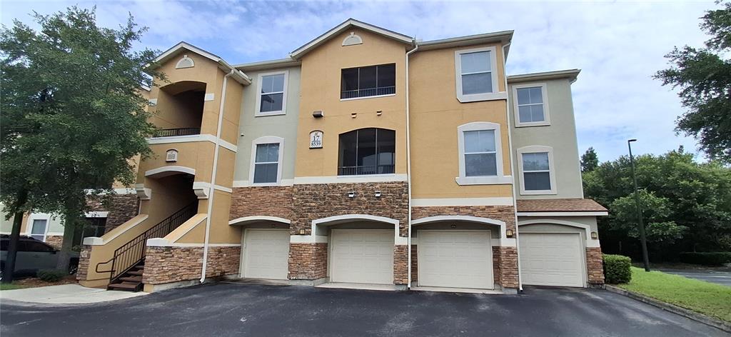 A three-story apartment building with tan stucco, stone veneer accents, and four ground-level garages — 8539 GATE PARKWAY W UNIT 1737, JACKSONVILLE, FL