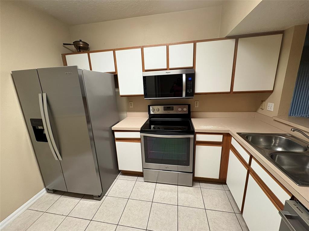 A kitchen features stainless steel appliances, white cabinets, and light-colored countertops over tiled floors — 9610 SEADALE COURT UNIT 102, RIVERVIEW, FL