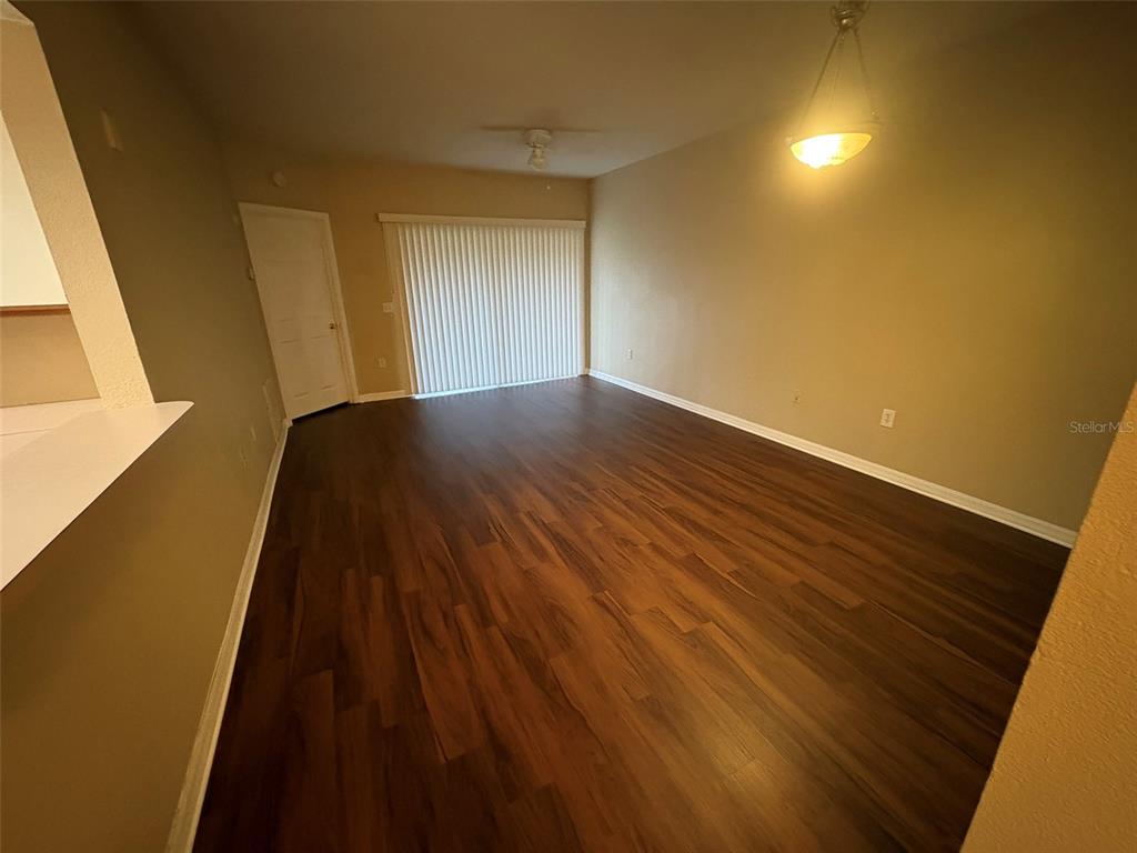 An empty living room features dark wood-look flooring, beige walls, and a sliding glass door — 9610 SEADALE COURT UNIT 102, RIVERVIEW, FL