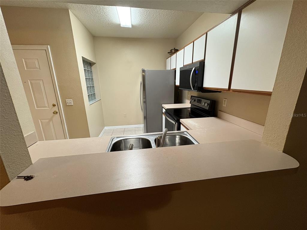 A kitchen features white cabinets, stainless steel appliances, a double sink, and beige countertops — 9610 SEADALE COURT UNIT 102, RIVERVIEW, FL