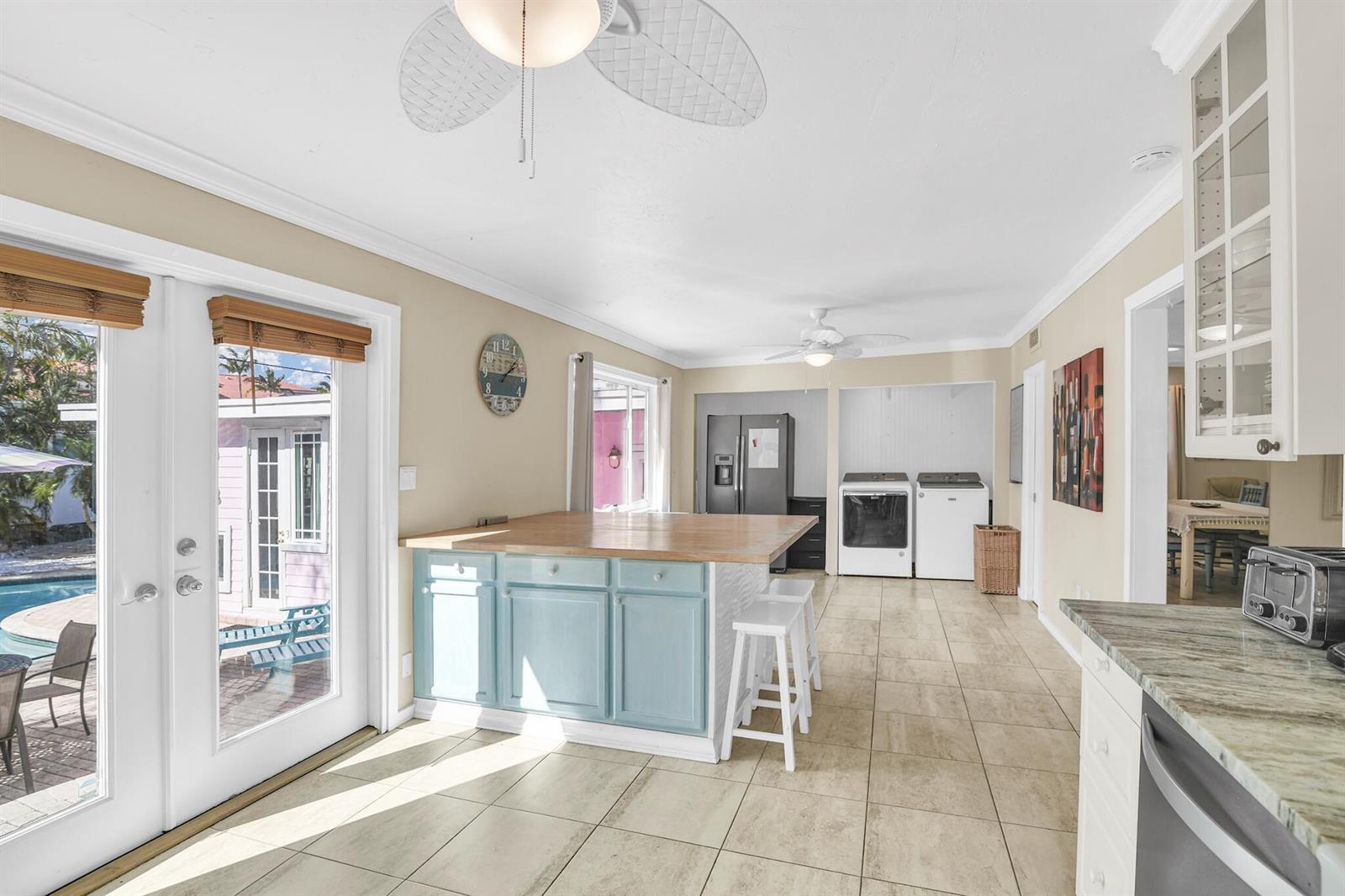 A kitchen features a light blue island with a wood countertop, tile flooring, and laundry appliances — 3218 Palm Drive, Delray Beach FL 33483, DELRAY BEACH, FL