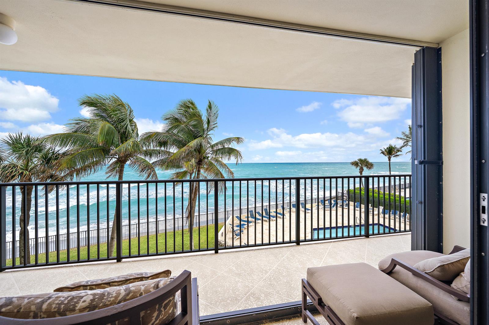 A balcony with outdoor furniture overlooks a swimming pool, palm trees, and the ocean — 200 Beach Road # 202, Tequesta FL 33469, TEQUESTA, FL