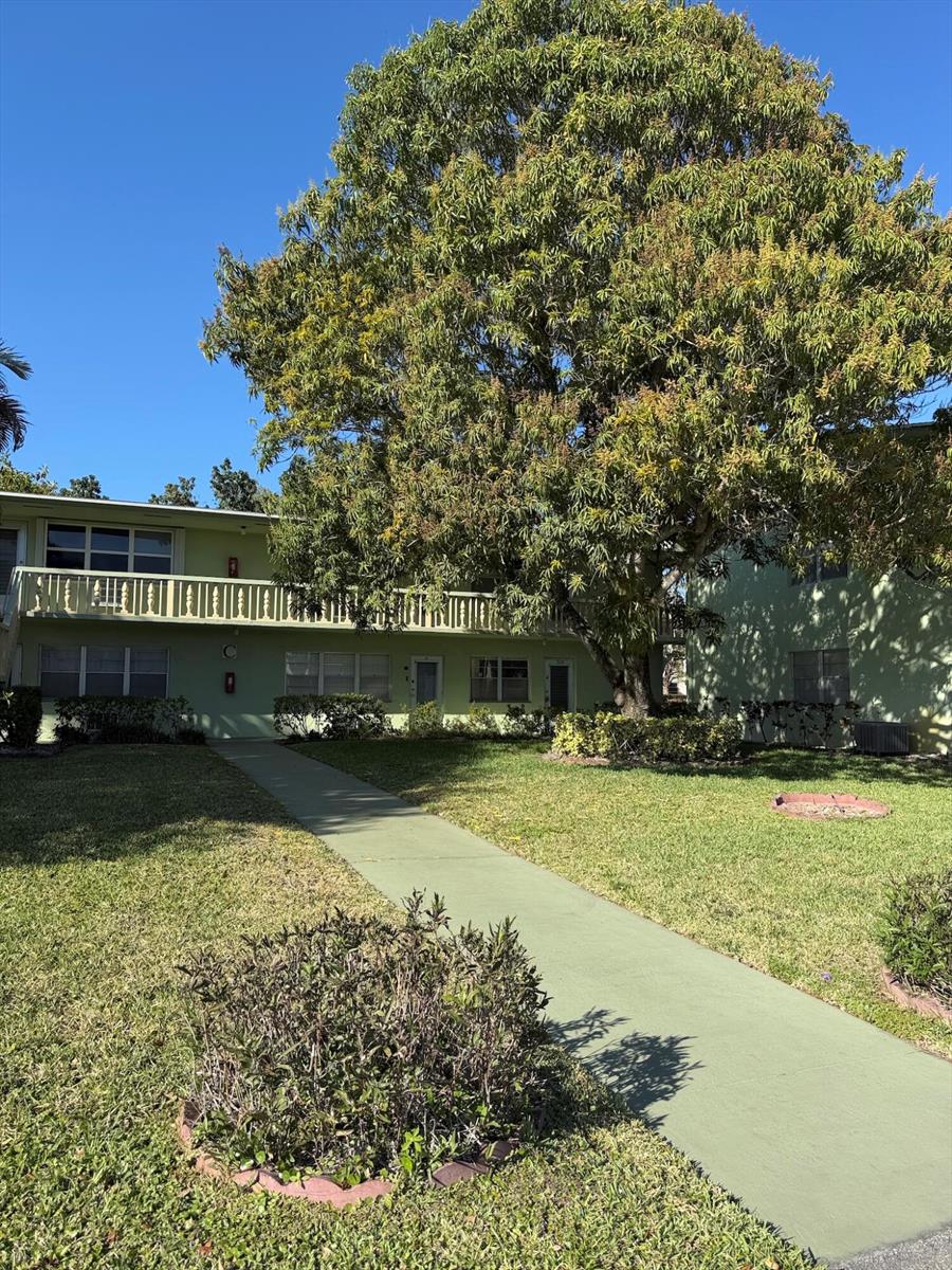 A two-story apartment building with a green exterior, a balcony, and a large tree — 64 Norwich C, West Palm Beach FL 33417, WEST PALM BEACH, FL