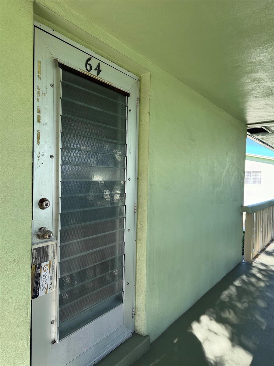 A light green exterior wall features a white screen door marked with the number 64 — 64 Norwich C, West Palm Beach FL 33417, WEST PALM BEACH, FL