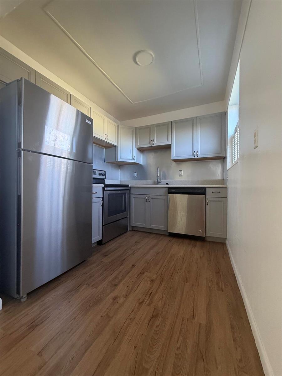 A galley kitchen features stainless steel appliances, grey cabinets, and light wood-look flooring — 64 Norwich C, West Palm Beach FL 33417, WEST PALM BEACH, FL
