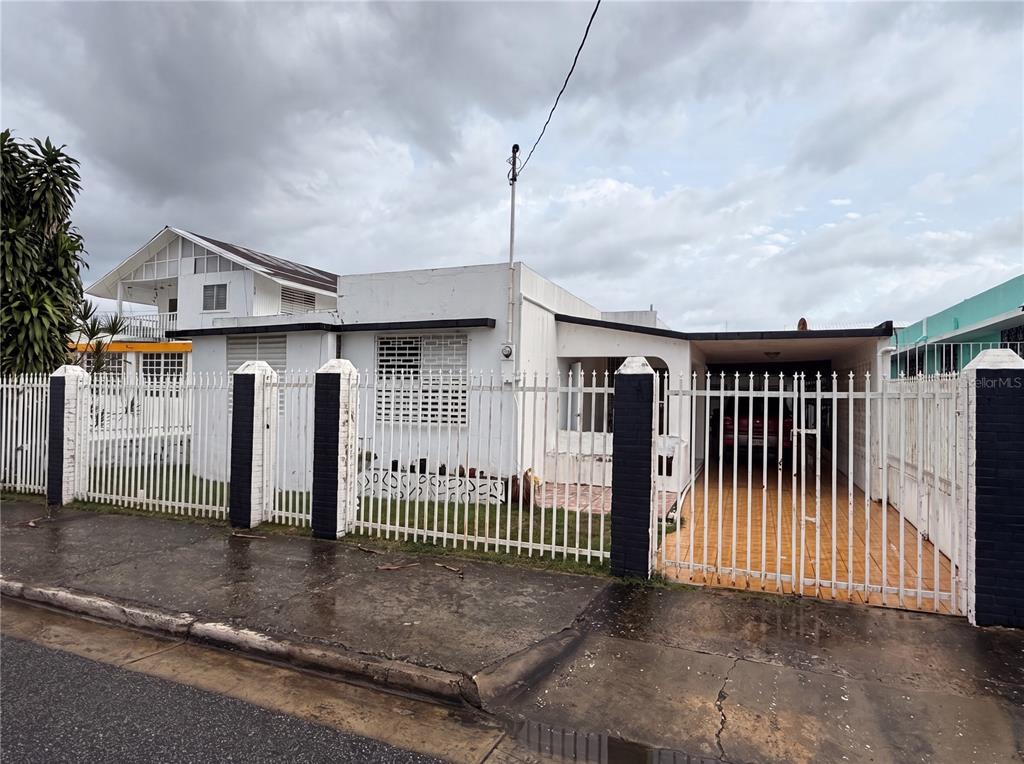 A white single-story house with a gated driveway and a metal fence in front — 187 ROMAGUERA STREET, MAYAGUEZ, PR