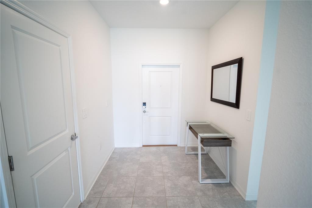 A tiled entryway features a white front door, a glass-topped console table, and a wall mirror — 4211 LITTLE OWL LANE, KISSIMMEE, FL