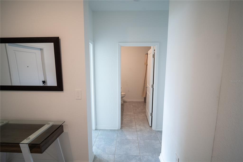 A hallway with tile flooring leads to a bathroom with a toilet and shower curtain — 4211 LITTLE OWL LANE, KISSIMMEE, FL
