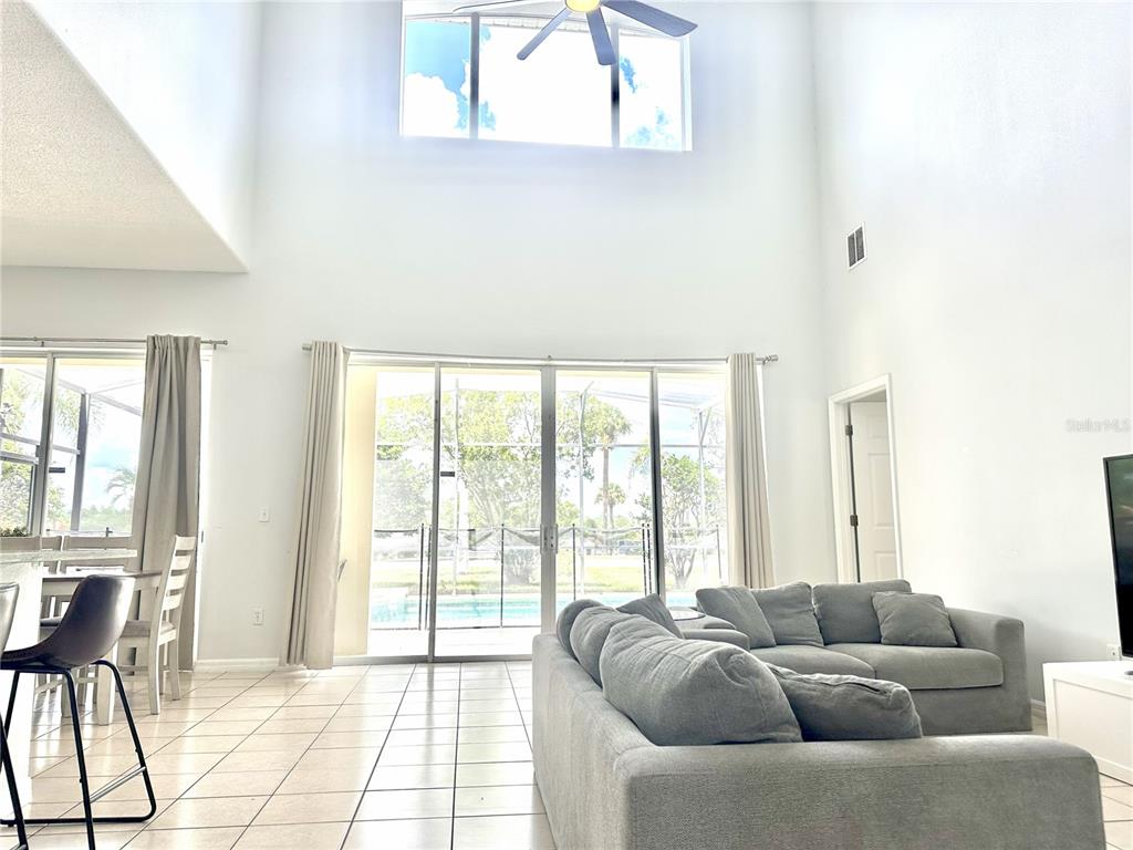 A living room with high ceilings, tile floors, a gray sectional sofa, and sliding glass doors — 1943 MORNING STAR DRIVE, CLERMONT, FL