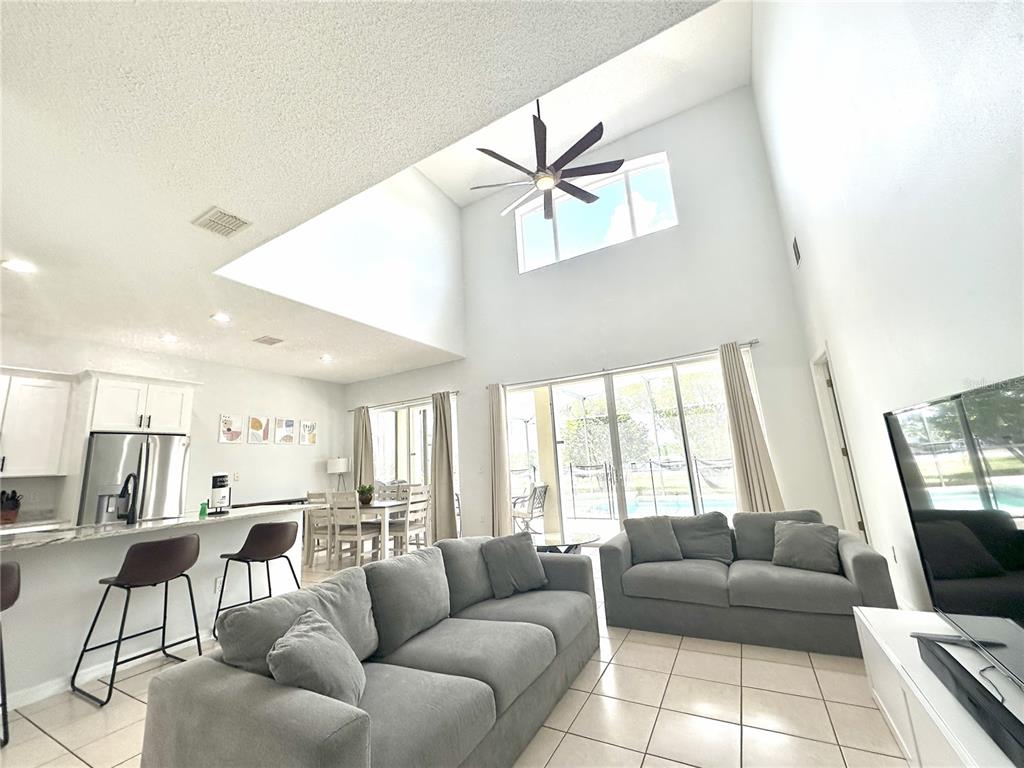 A living room with high ceilings, a ceiling fan, tile floors, and a kitchen area — 1943 MORNING STAR DRIVE, CLERMONT, FL