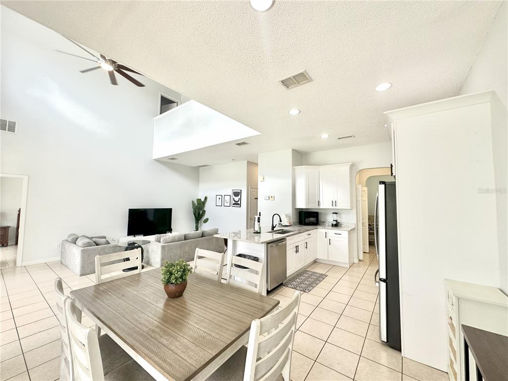 An open-concept kitchen and dining area features white cabinetry, tile flooring, and vaulted ceilings — 1943 MORNING STAR DRIVE, CLERMONT, FL