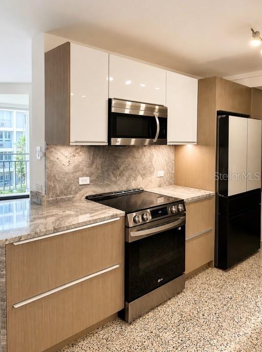 A modern kitchen features light wood cabinetry, white upper cabinets, stainless steel appliances, and stone countertops — 185–187 PINE GROVE STREET, CAROLINA, PR