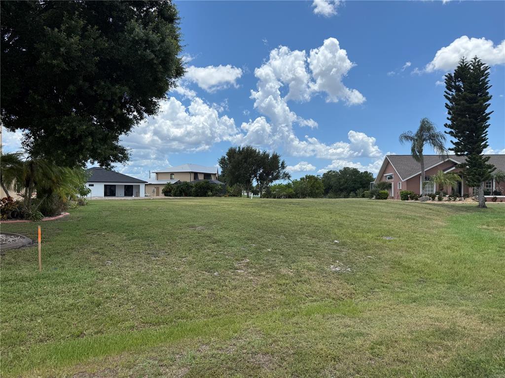 A grassy vacant lot sits between two residential houses under a blue sky with clouds — 25283 OJIBWAY COURT, PUNTA GORDA, FL