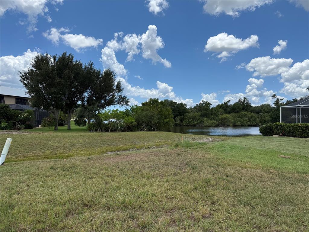 A grassy lot overlooks a pond with trees and a neighboring house in the distance — 25283 OJIBWAY COURT, PUNTA GORDA, FL
