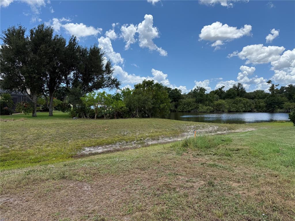 A grassy lot slopes down toward a pond surrounded by trees under a blue sky — 25283 OJIBWAY COURT, PUNTA GORDA, FL