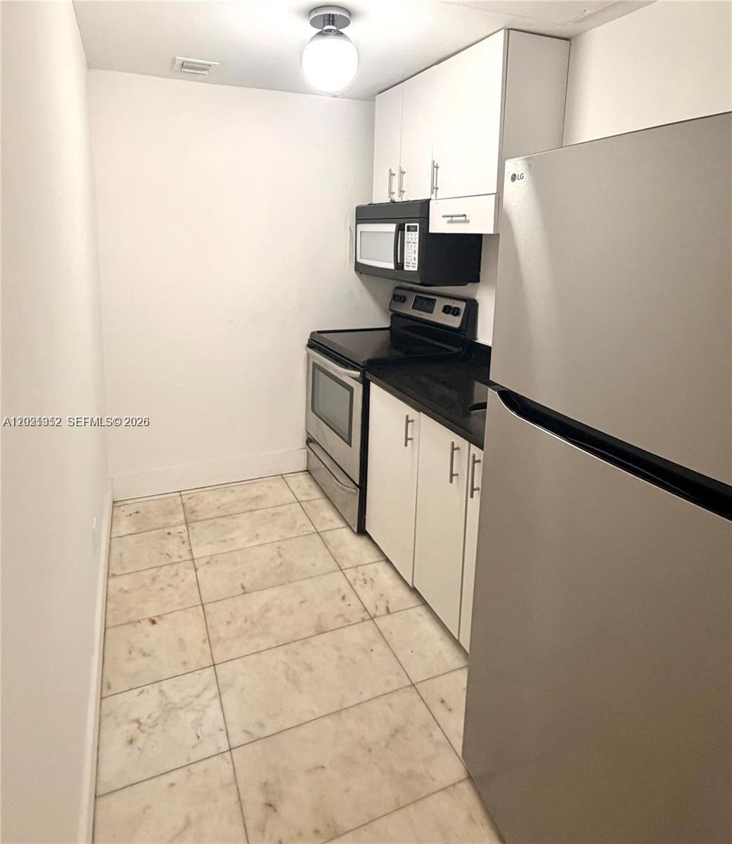 This galley kitchen features white cabinets, stainless steel appliances, and light-colored tile flooring — 801 8th St # 104, Miami Beach FL 33139, MIAMI BEACH, FL