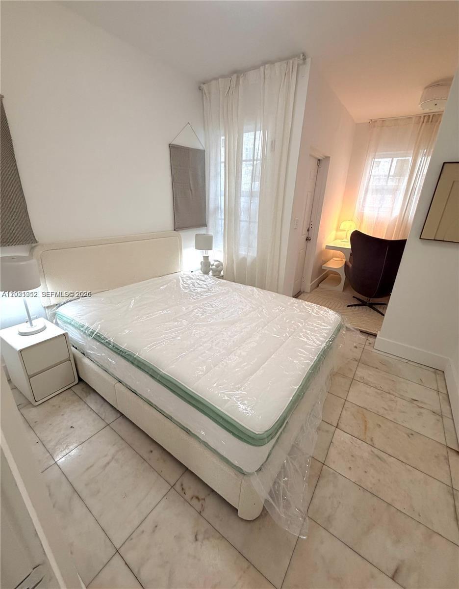 A bedroom features a bed with a plastic-covered mattress, tile flooring, and a small desk area — 801 8th St # 104, Miami Beach FL 33139, MIAMI BEACH, FL