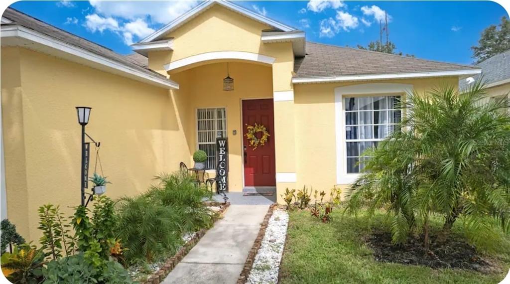 A yellow single-story house with a red front door, a walkway, and a palm tree — 238 SUNSET VIEW DRIVE, DAVENPORT, FL