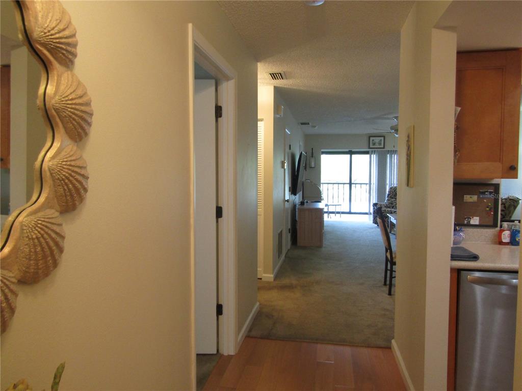 A hallway with wood-look flooring leads into a carpeted living area with a sliding glass door — 2961 TAYWOOD MEADOWS UNIT 26, SARASOTA, FL