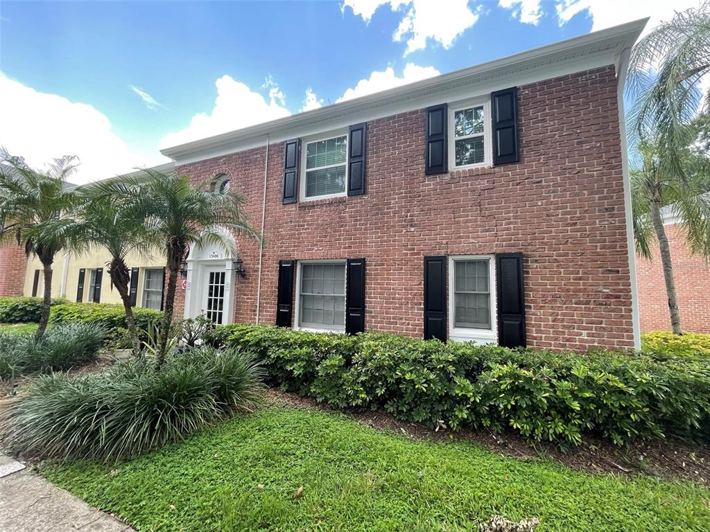 A two-story brick building features black shutters, white window frames, and a landscaped front yard — 13686 ORANGE SUNSET DR UNIT 201, TAMPA, FL