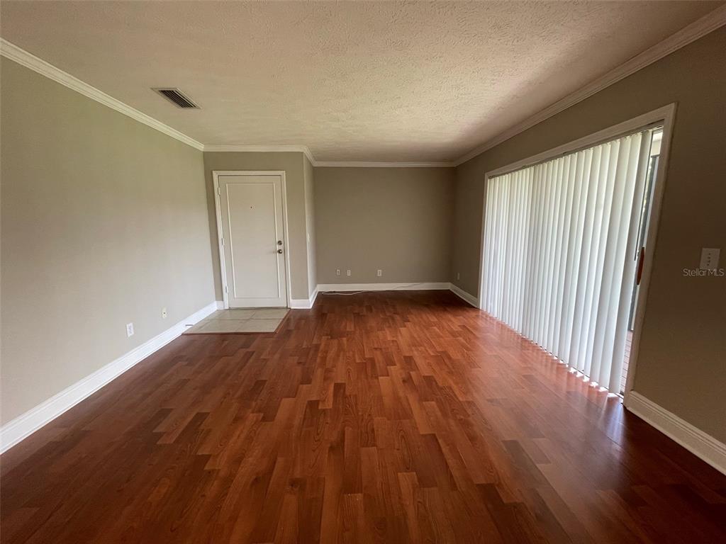 An empty living room features hardwood floors, light-colored walls, a white door, and vertical blinds — 13686 ORANGE SUNSET DR UNIT 201, TAMPA, FL