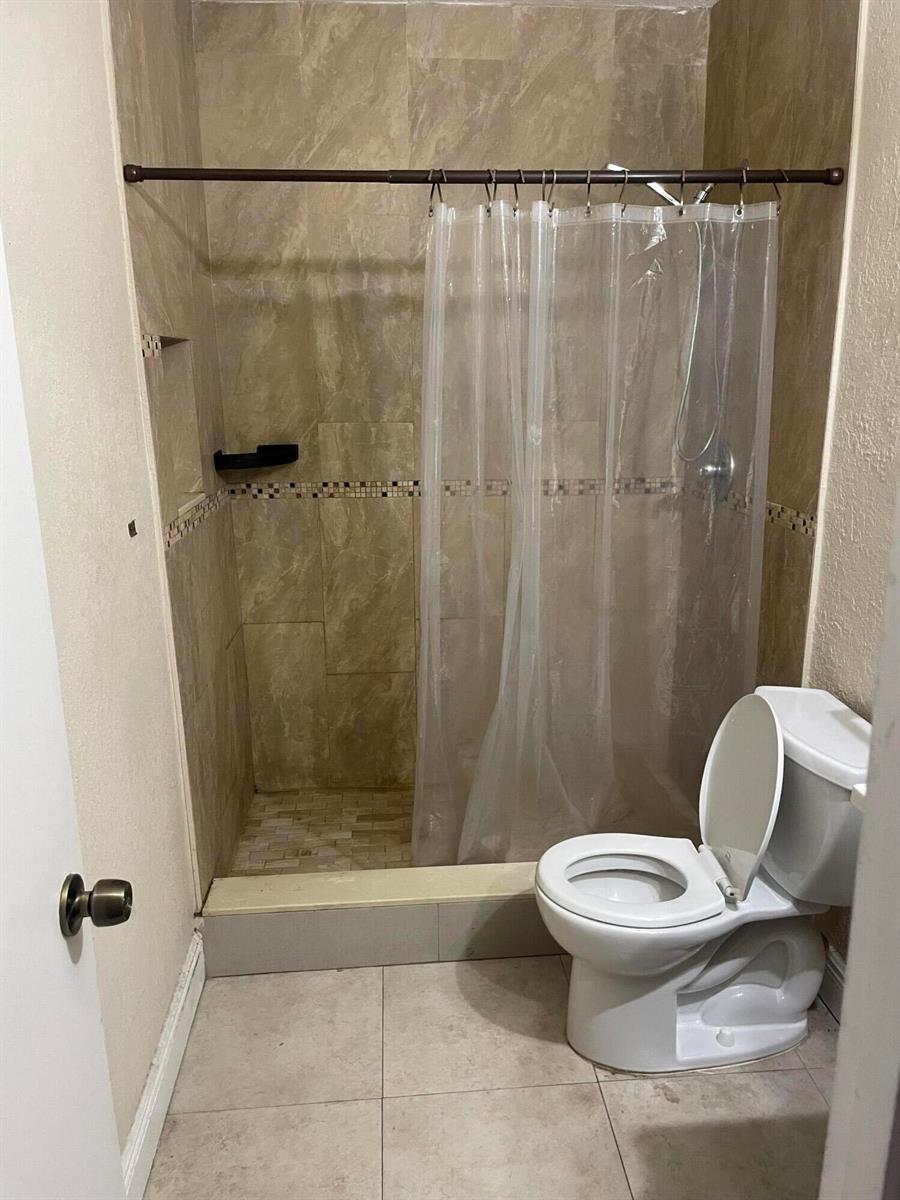 A bathroom features a tiled walk-in shower with a curtain and a white toilet — 8249 Fairway Road, Sunrise FL 33351, SUNRISE, FL
