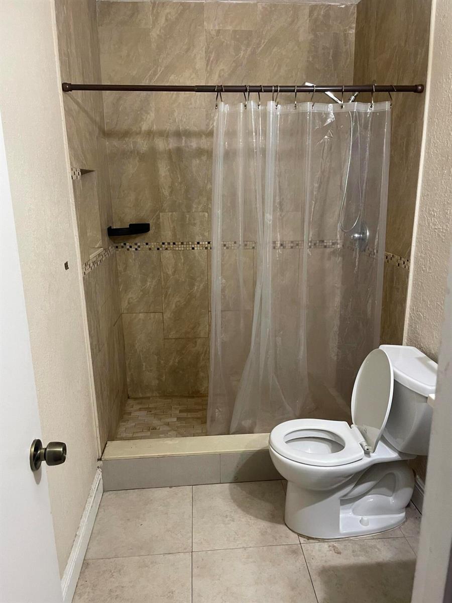 A bathroom features a tiled walk-in shower with a curtain and a white toilet — 8249 Fairway Road, Sunrise FL 33351, SUNRISE, FL