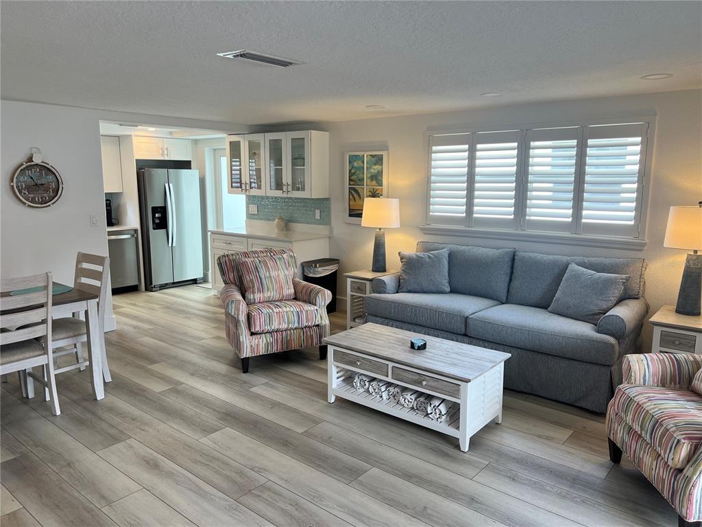 A living room and dining area feature light wood-look flooring, a gray sofa, and patterned chairs — 6154 MIDNIGHT PASS ROAD UNIT A15, SARASOTA, FL