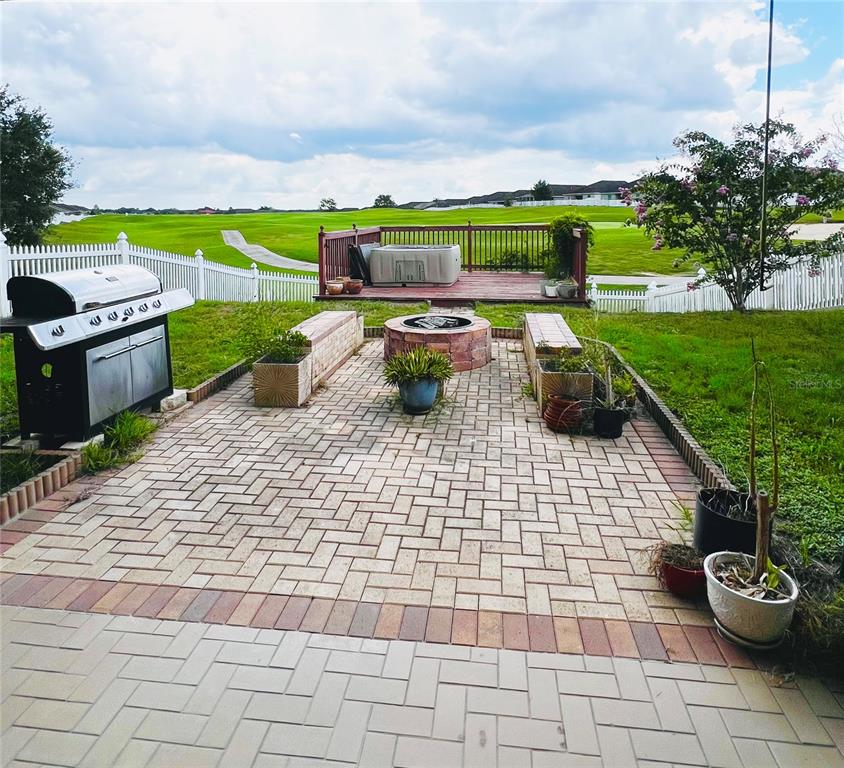 A paved patio features a fire pit, built-in benches, a grill, and a raised wooden deck — 30722 SATINLEAF RUN, BROOKSVILLE, FL
