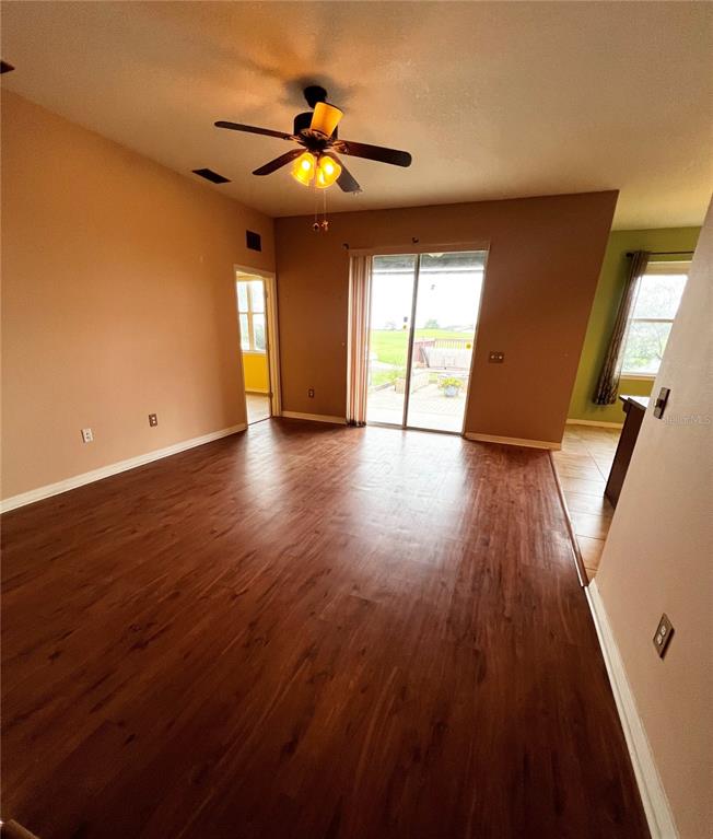 A living room with wood-look flooring, a ceiling fan, and sliding glass doors to a patio — 30722 SATINLEAF RUN, BROOKSVILLE, FL