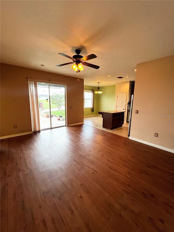 A living room with wood-look flooring, a ceiling fan, and a sliding glass door — 30722 SATINLEAF RUN, BROOKSVILLE, FL