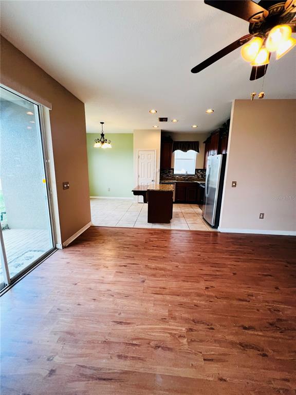 A room with wood-look flooring leads to a kitchen featuring dark cabinets and tile floors — 30722 SATINLEAF RUN, BROOKSVILLE, FL