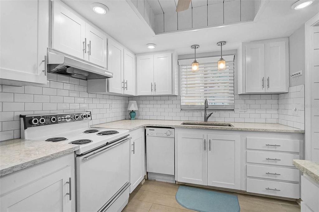 A bright kitchen features white cabinets, a white stove, a dishwasher, and a subway tile backsplash — 3585 LAKE BAYSHORE DRIVE UNIT J-301, BRADENTON, FL