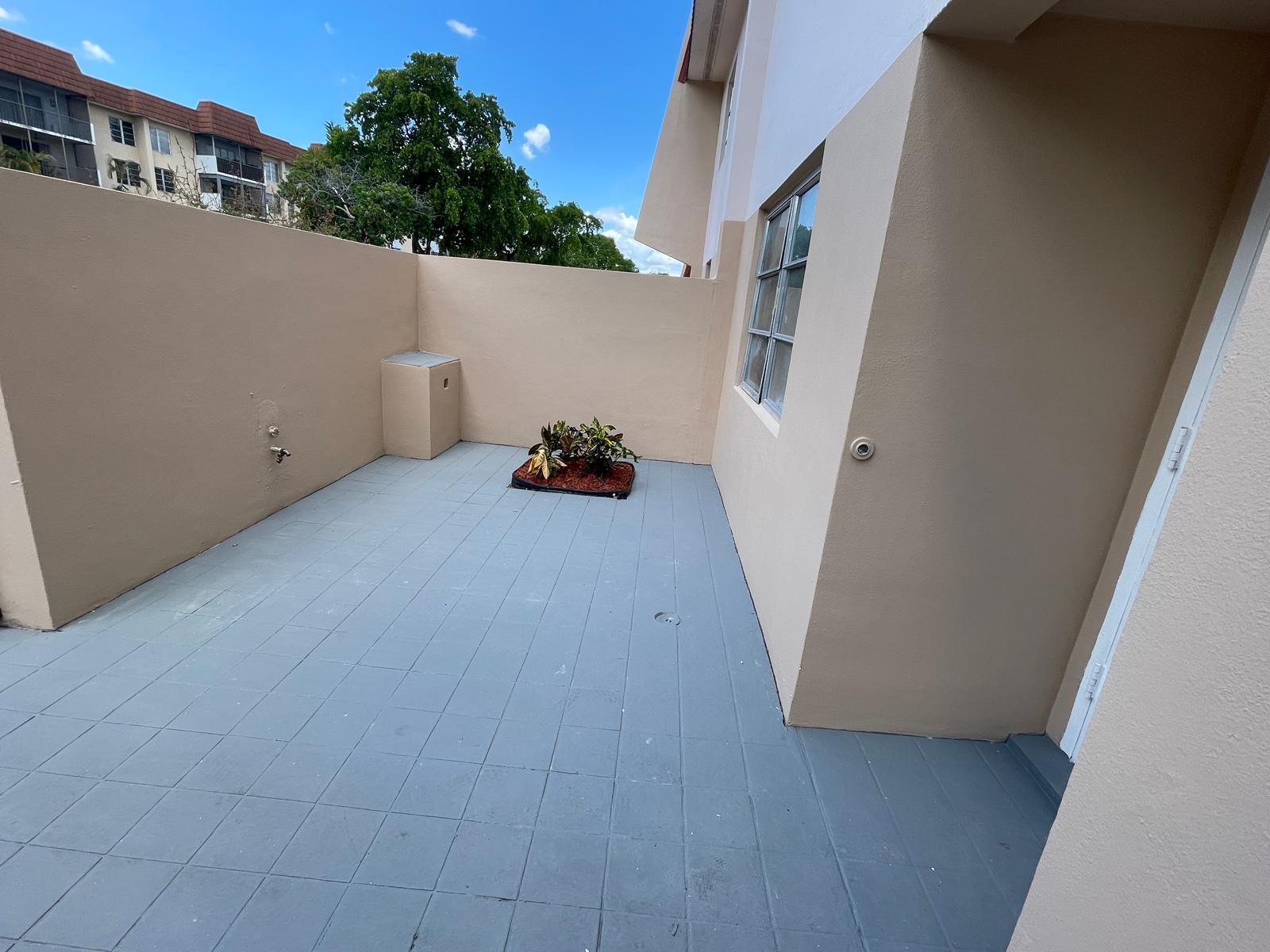 An outdoor patio features gray tiled flooring, a small garden bed, and beige stucco walls — 4140 Inverrary Drive # 15e, Lauderhill FL 33319, LAUDERHILL, FL