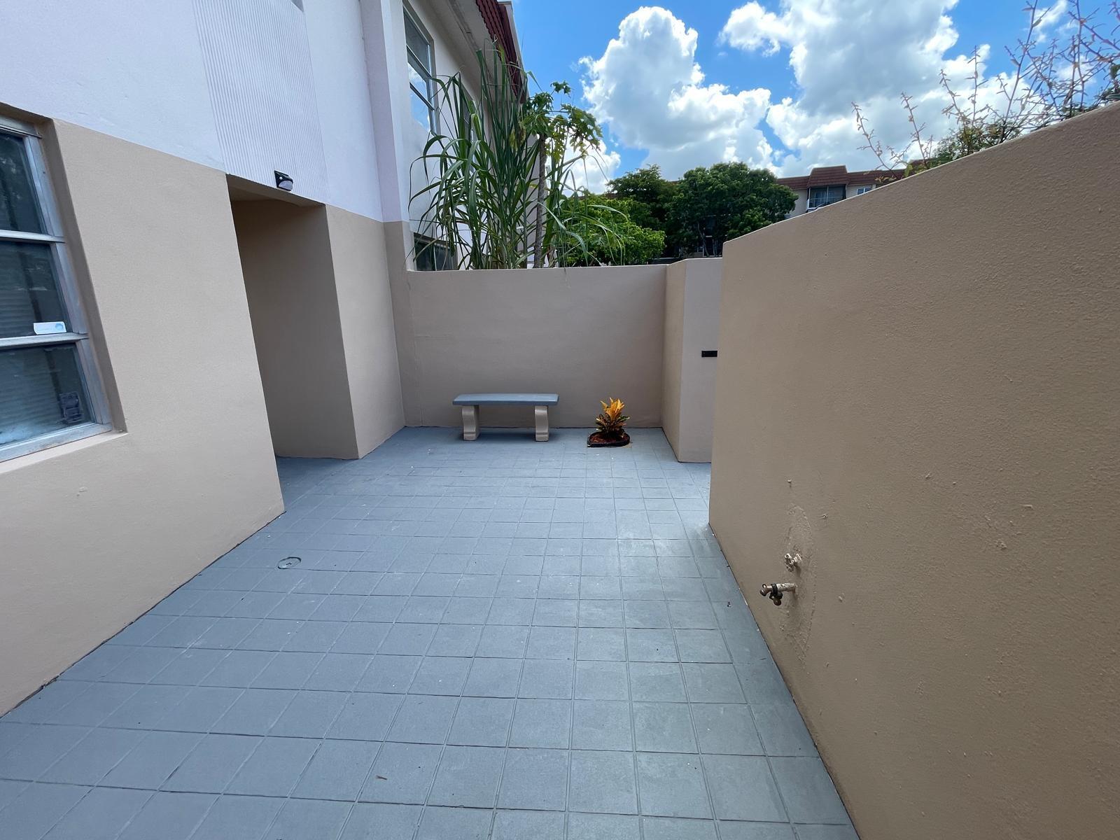 A paved outdoor patio features a small bench, a potted plant, and tan walls — 4140 Inverrary Drive # 15e, Lauderhill FL 33319, LAUDERHILL, FL