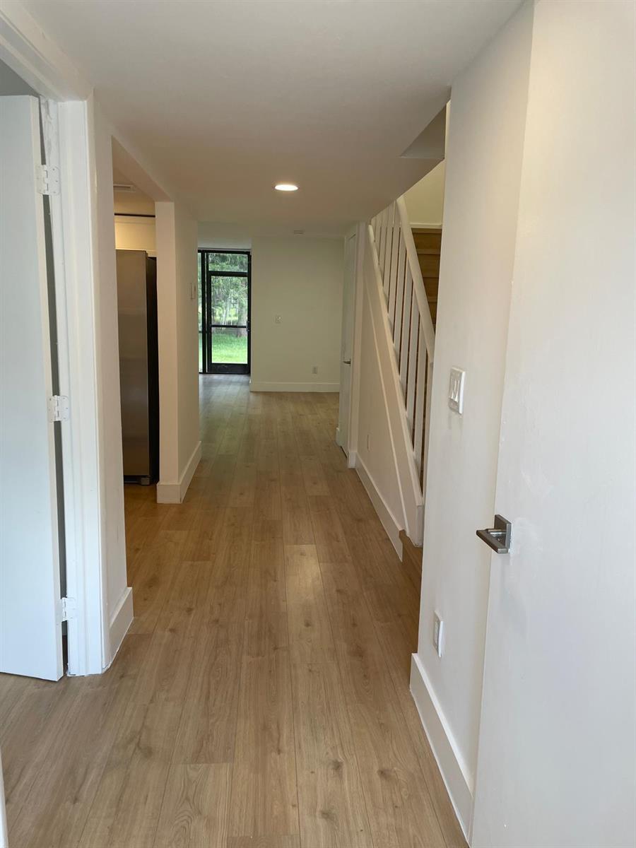 A hallway with light wood flooring leads past a staircase toward a glass exterior door — 4140 Inverrary Drive # 15e, Lauderhill FL 33319, LAUDERHILL, FL