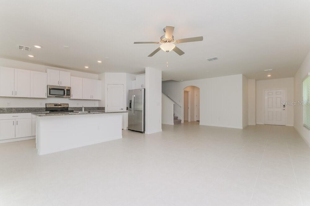 An open-concept kitchen with white cabinets and stainless steel appliances overlooks a spacious living area — 7337 SPRING SNOWFLAKE AVENUE, TAMPA, FL