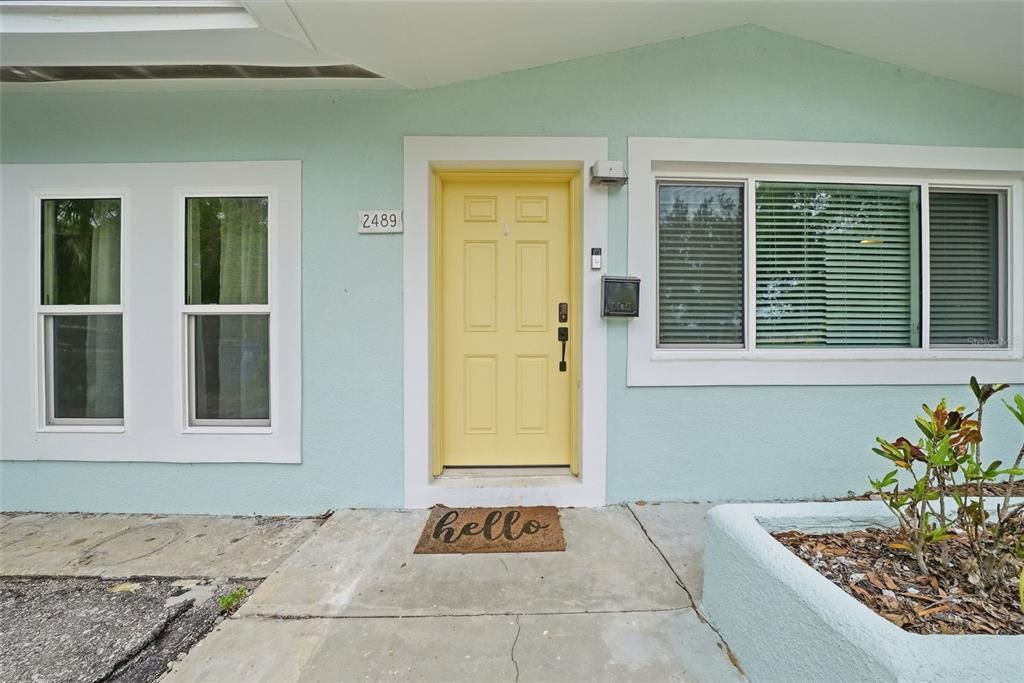 A light blue house exterior features a yellow front door and a hello doormat — 2489 58TH STREET N, ST PETERSBURG, FL