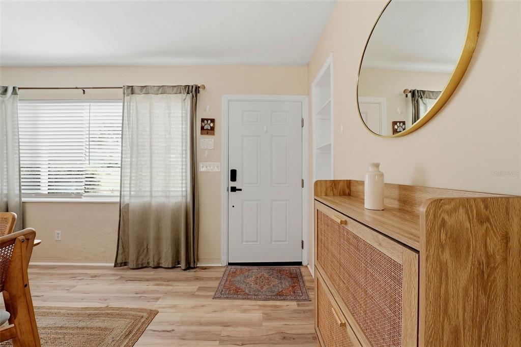 An entryway features a white door, a wooden cabinet, a round mirror, and wood-look flooring — 2489 58TH STREET N, ST PETERSBURG, FL