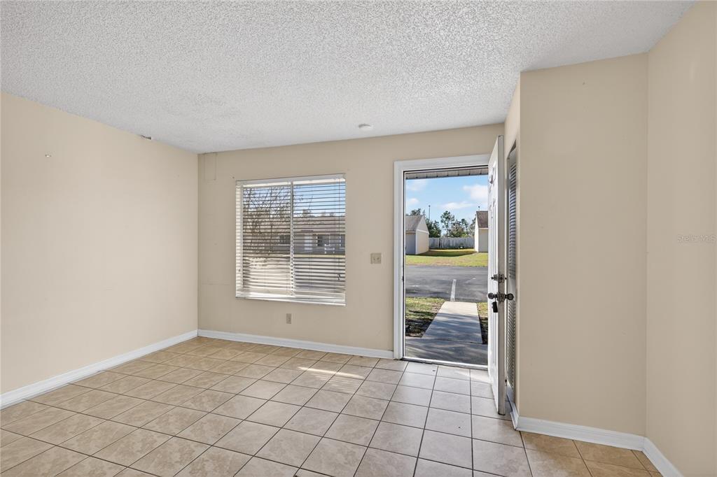 An empty room with beige walls, tile flooring, a window with blinds, and an open door — 30034 TAVARES RIDGE BOULEVARD UNIT 1, TAVARES, FL