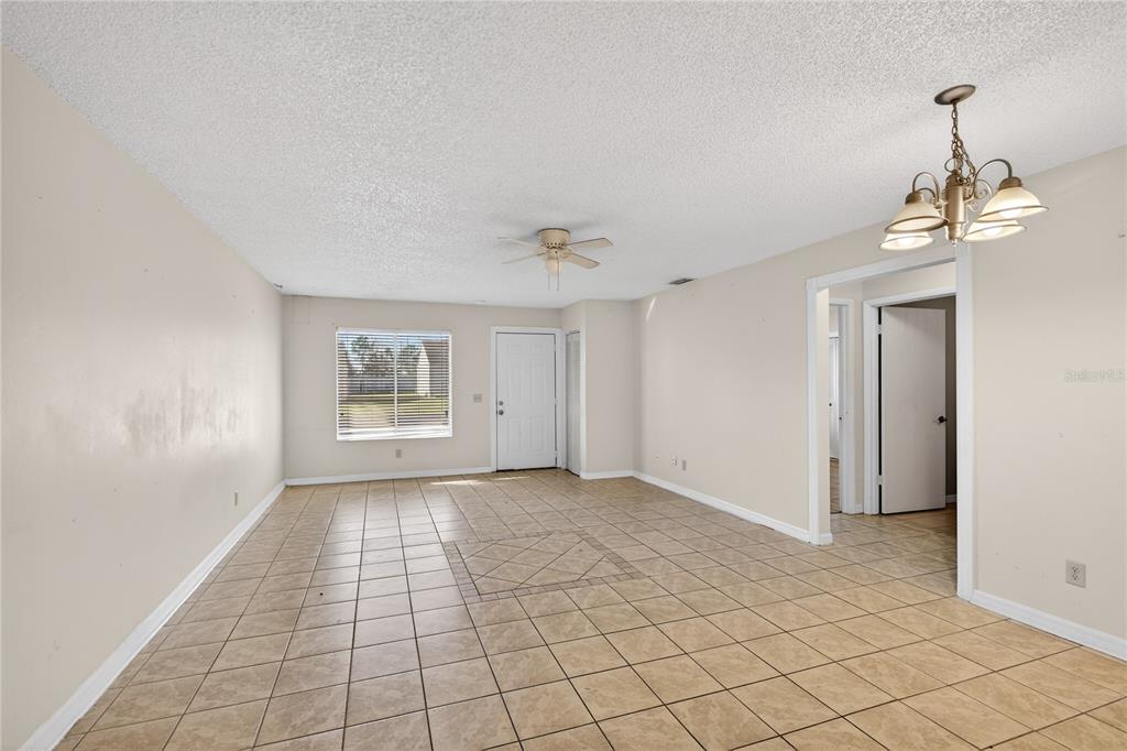 An empty living room features beige tile flooring, a ceiling fan, and a chandelier — 30034 TAVARES RIDGE BOULEVARD UNIT 1, TAVARES, FL