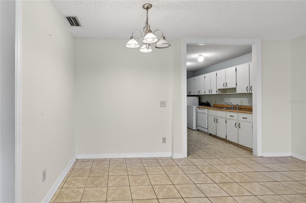 A dining area with tile flooring and a chandelier leads into a kitchen with white cabinets — 30034 TAVARES RIDGE BOULEVARD UNIT 1, TAVARES, FL