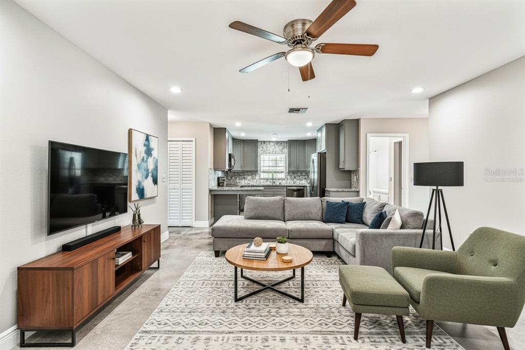 A living room with a grey sectional, wooden coffee table, and open kitchen in the background — 1101 81ST AVENUE N, ST PETERSBURG, FL