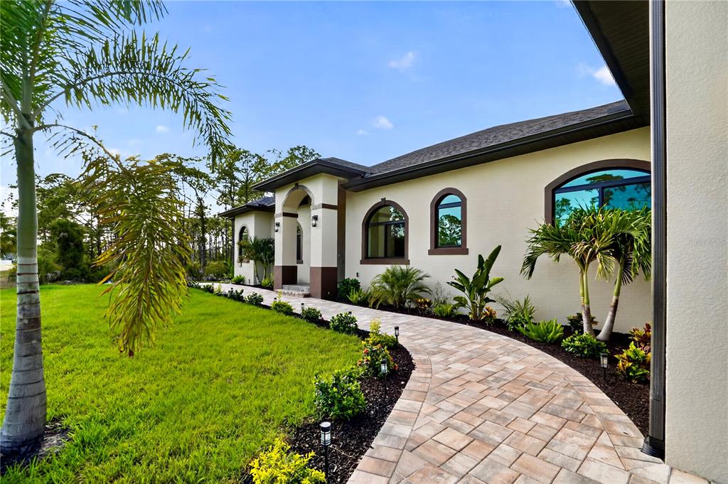 A paved walkway leads to the entrance of a house with arched windows and landscaping — 12252 DIETRICH AVENUE, PORT CHARLOTTE, FL