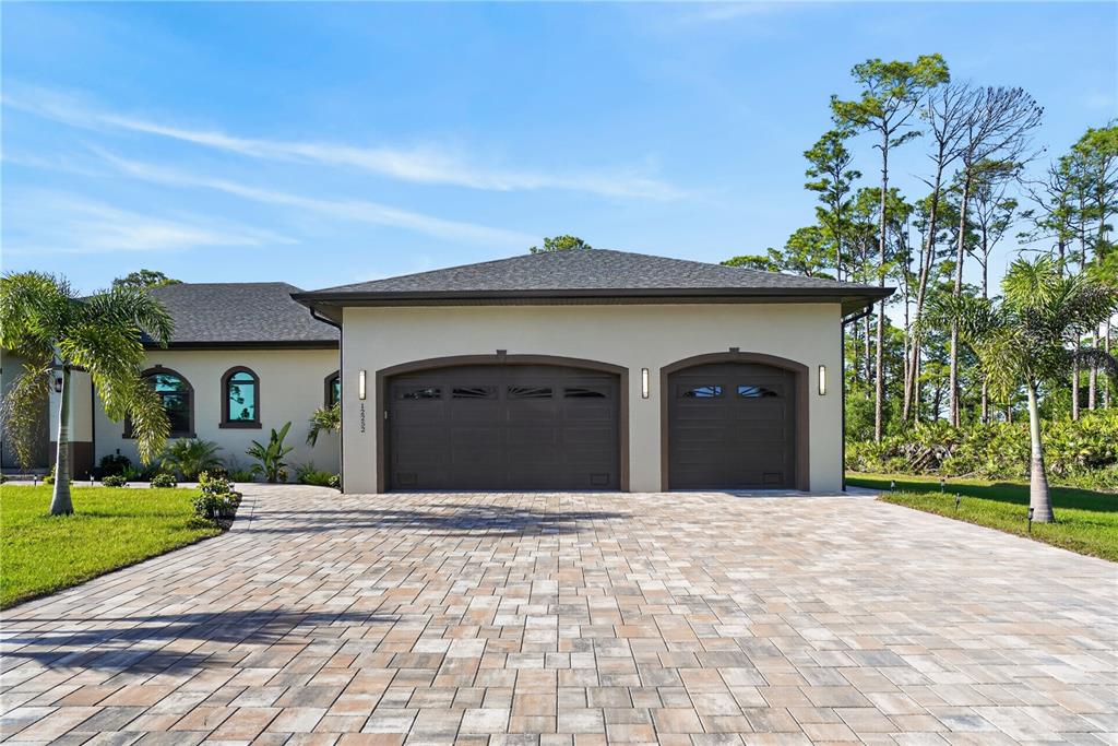 A beige house exterior features a paver driveway, two arched garage doors, and palm trees — 12252 DIETRICH AVENUE, PORT CHARLOTTE, FL