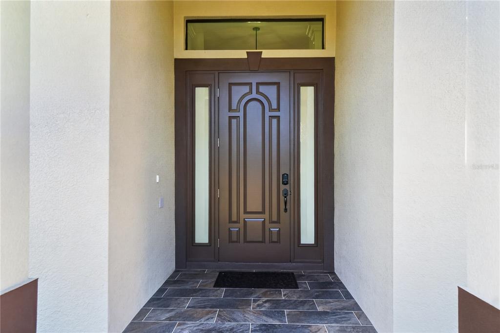 A dark brown front door with side lights and a transom window sits under a porch — 12252 DIETRICH AVENUE, PORT CHARLOTTE, FL
