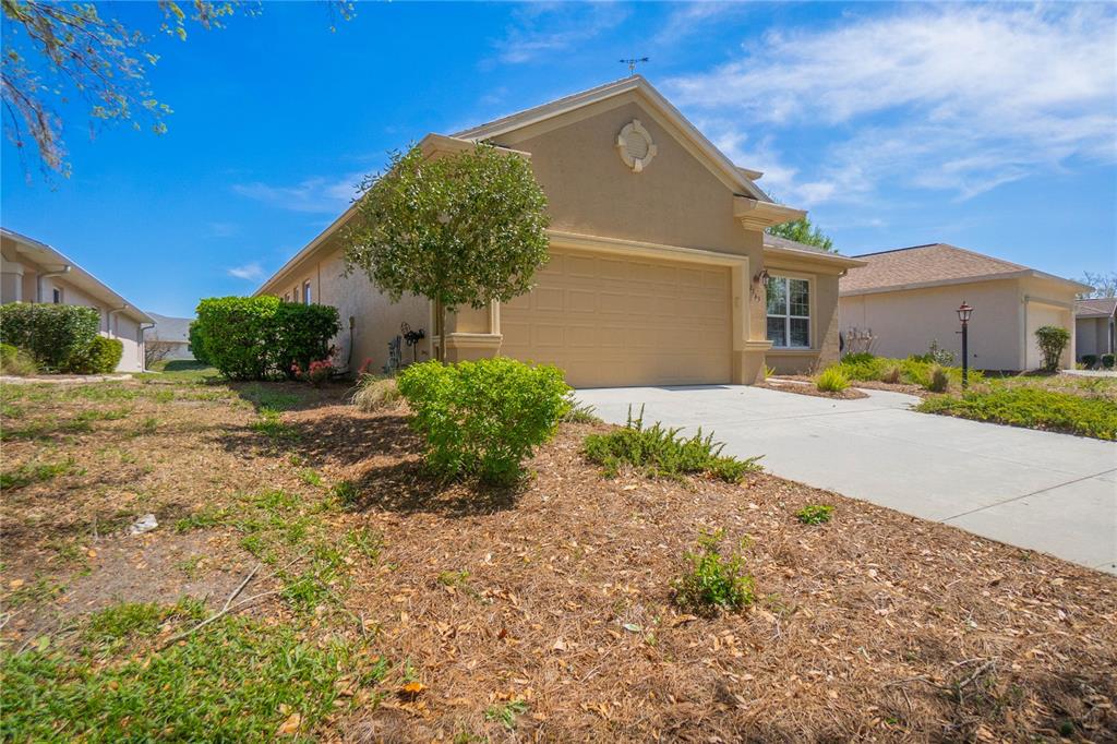 A tan single-story house features a two-car garage, a concrete driveway, and landscaped front yard — 2163 N BRENTWOOD CIRCLE, LECANTO, FL